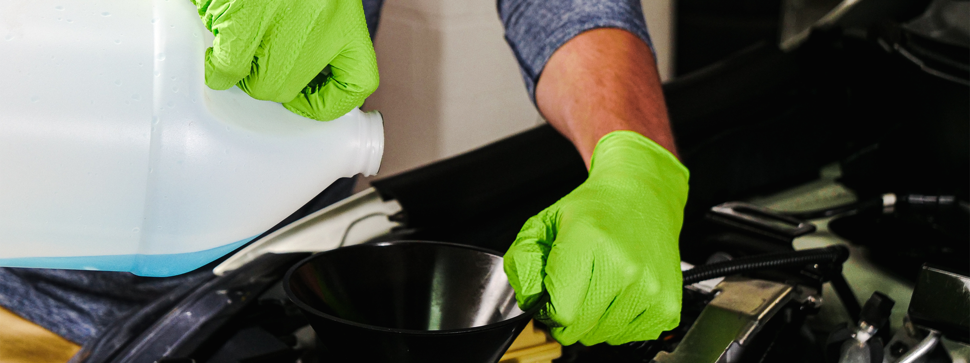 A pair of hands wearing python grip nitrile gloves pouring blue liquid into a funnel.