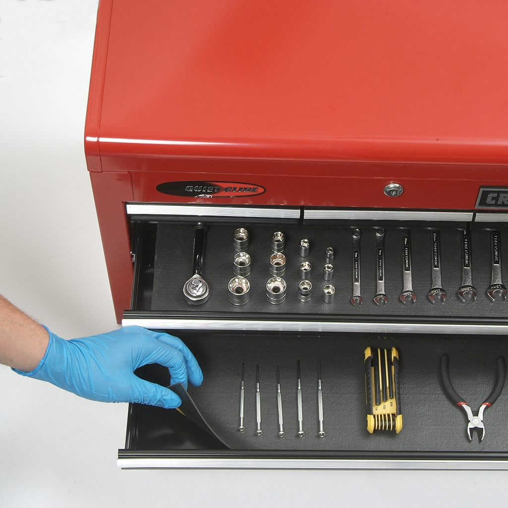 A gloved hand lifting up the corner of a drawer liner in a toolbox