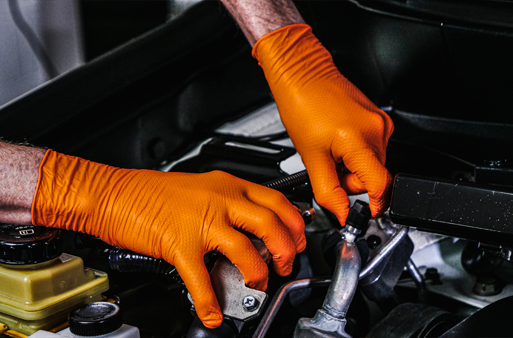 a pair of hand wearing orange nitrile gloves while working on an engine.