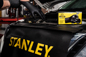 A pair of hands putting on Lion Grip Gloves next to a box of Lion Grip Gloves sitting on a Professional Fender Cover with the Stanley logo